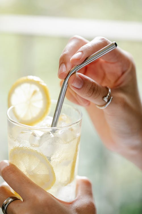 Crop anonymous female touching cocktail tube with hands on blurred background in daylight