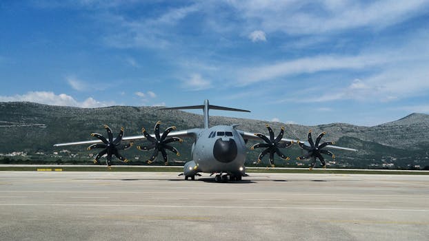 A military aircraft with propellers parked on a runway against a scenic hill backdrop.