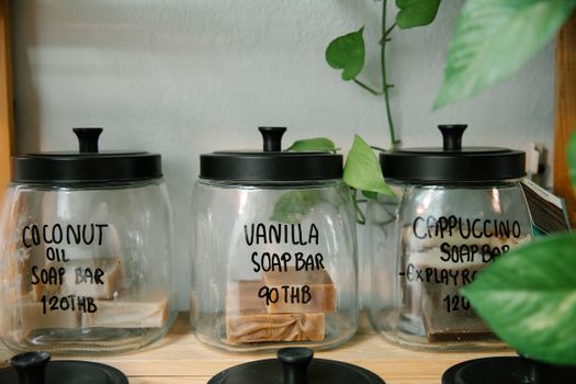 Collection of various handmade bar soap in plastic jars with black lids placed on wooden surface