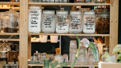 Collection of various glass jars with different dry food and glassware placed on wooden shelf