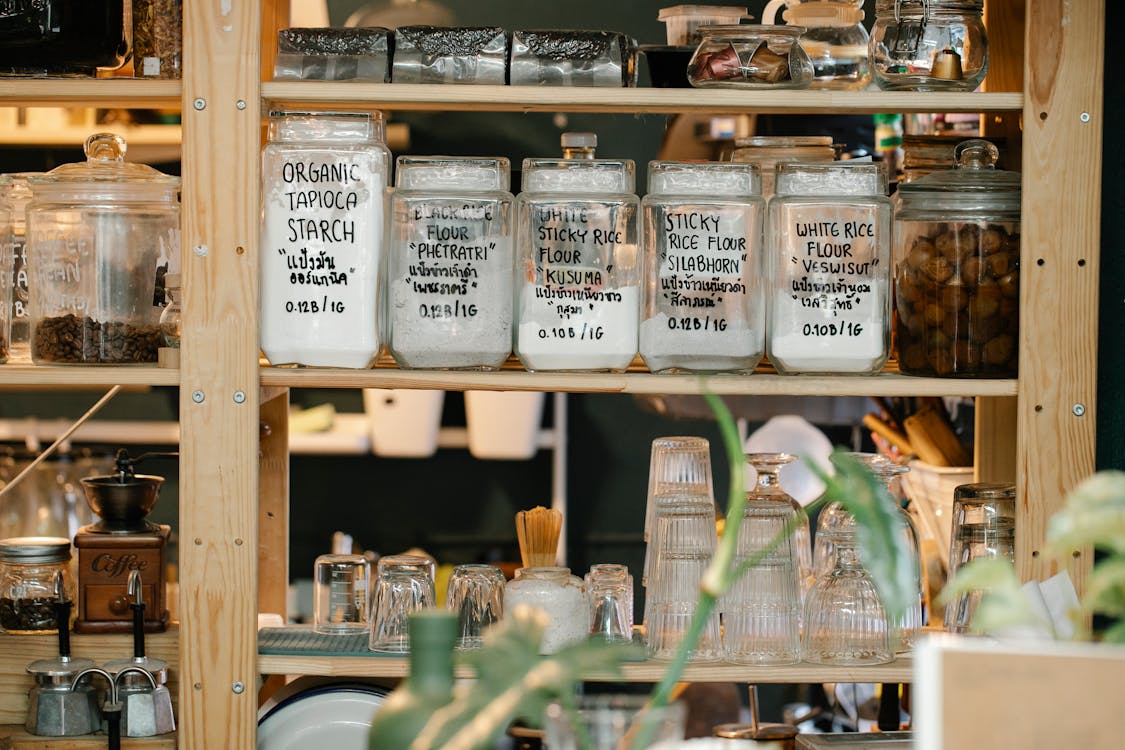 Glass Jars with Dry Food and Glassware on Shelves