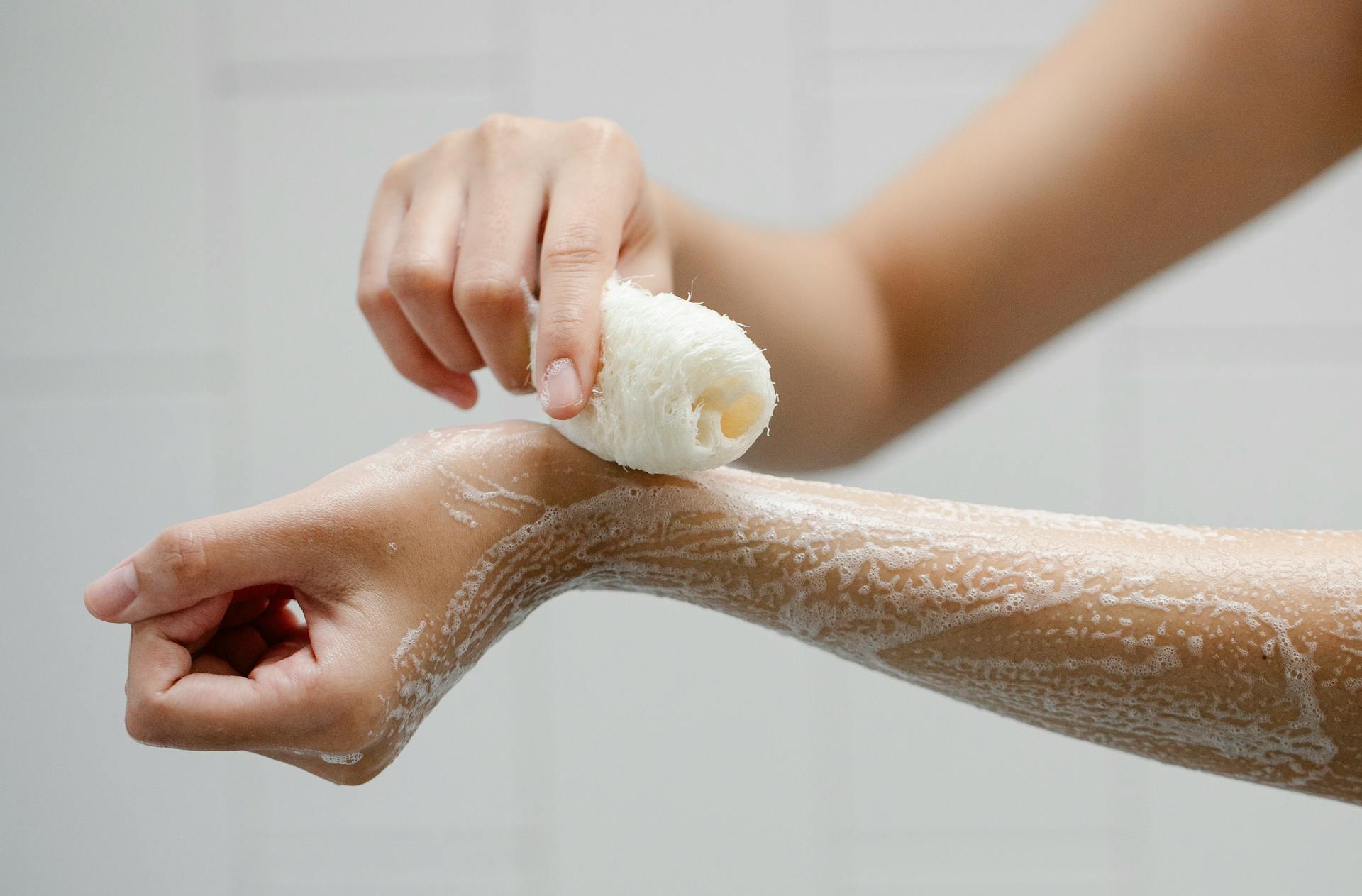 Crop anonymous person using wisp washing arms with soap foam during hygienic procedure