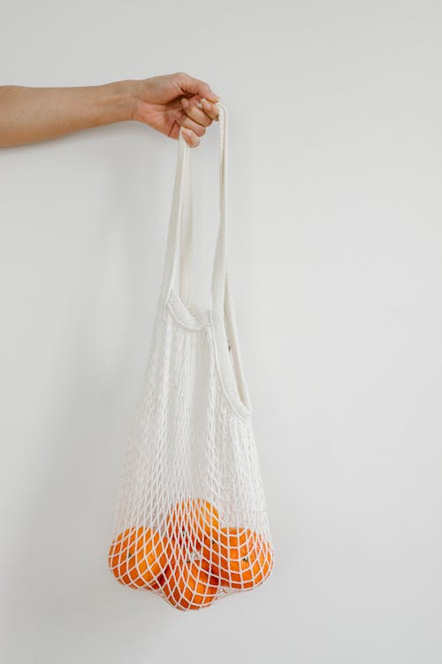 Crop person with oranges in string bag