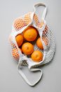 Top view of fresh oranges placed in white eco friendly string bag on white surface