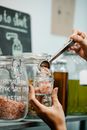 Crop anonymous tester putting spice from big transparent container into glass jar in supermarket