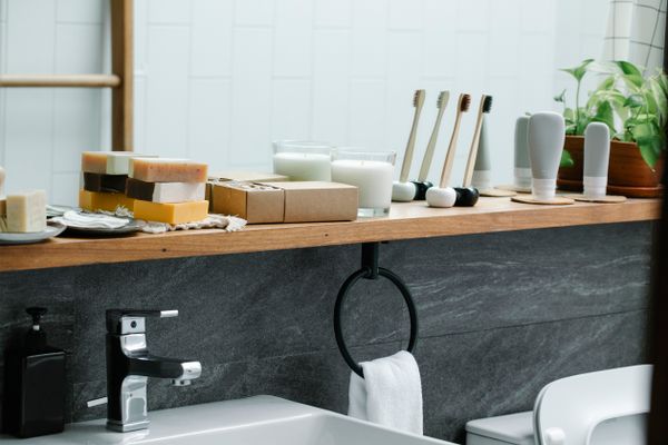 Small bathroom with a wooden wall shelf holding neatly arranged toiletries beside a mirror