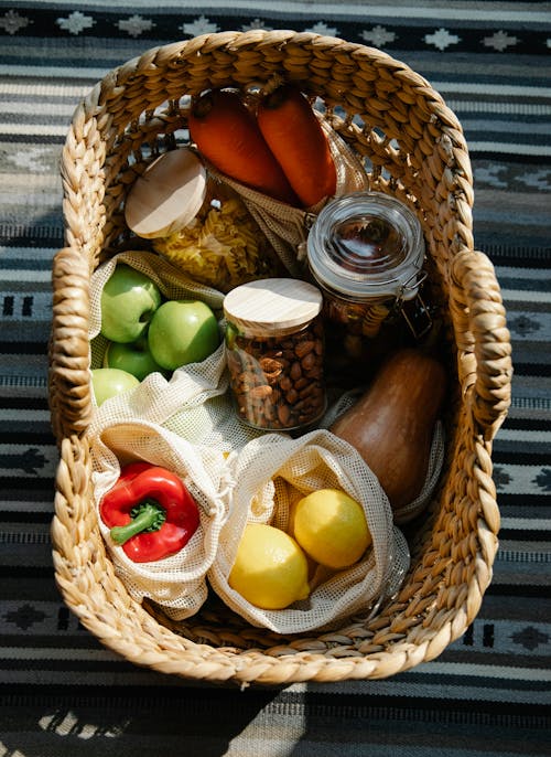 Free From above of wicker basket with vegetables and fruits placed in eco bags and glass jars with products in sunny day Stock Photo