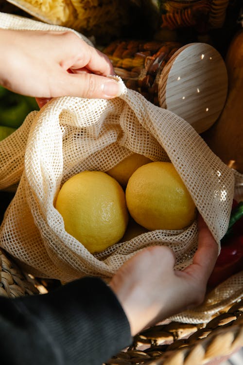 Free From above of crop person opening eco friendly bag with fresh ripe lemons placed in wicker basket Stock Photo