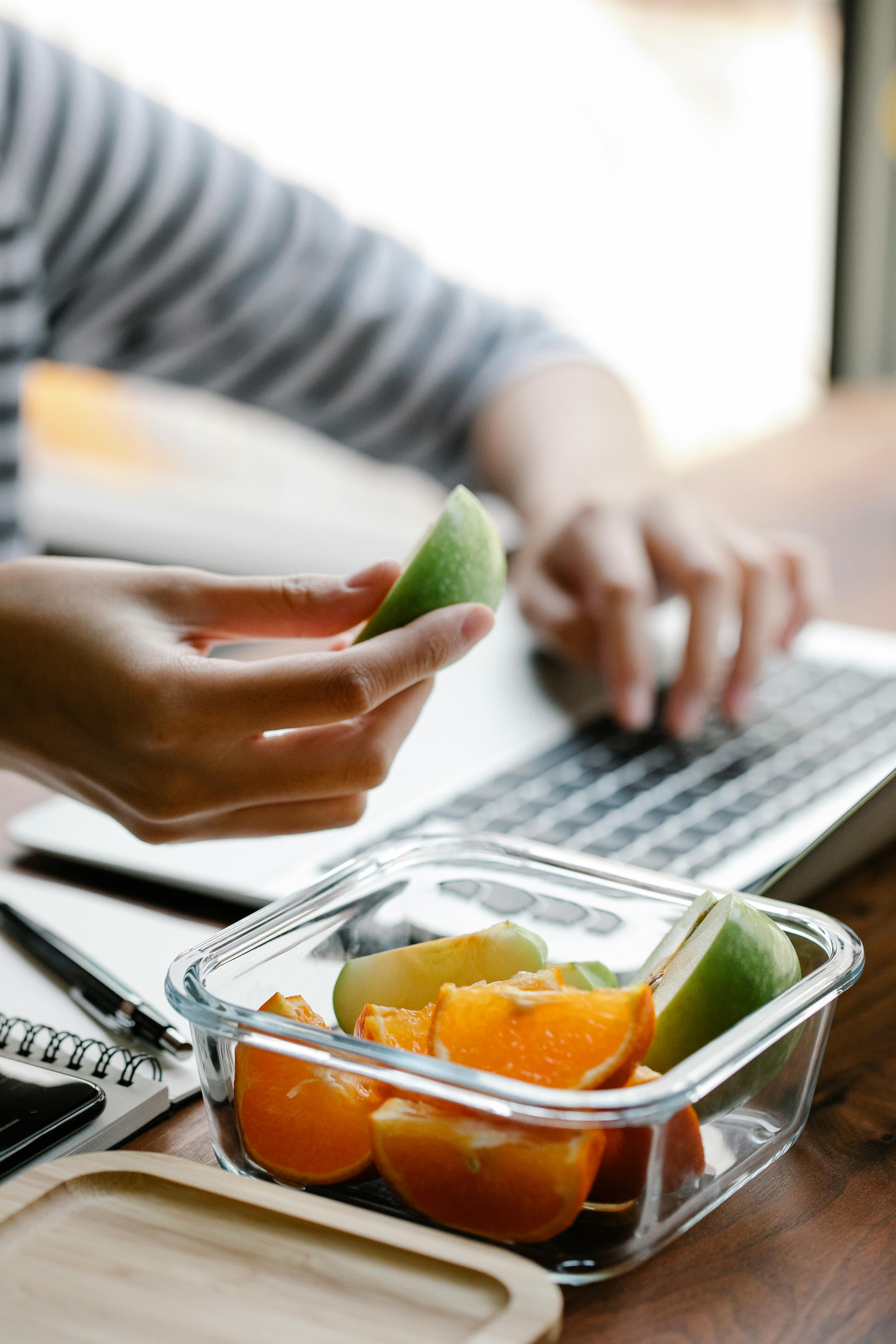 crop woman with fruits in container placed near laptop