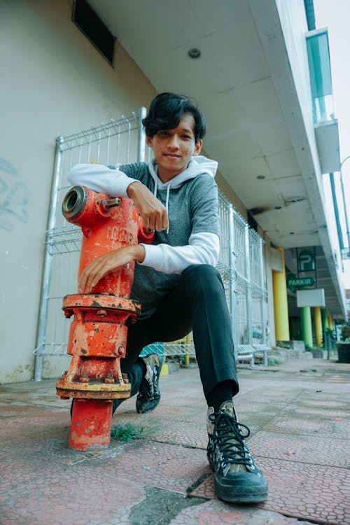 Confident young Asian male millennial sitting on haunches on street near fire hydrant