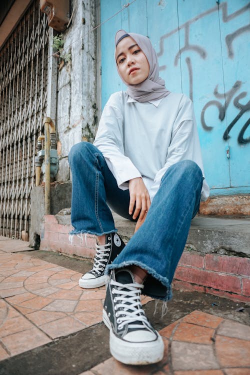 From below of Muslim female in jeans looking at camera on street with graffiti