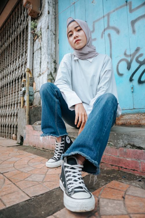 Free From below of Muslim female in jeans looking at camera on street with graffiti Stock Photo
