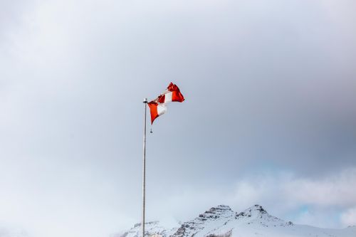 Free A Canadian flag on a pole with snow-covered mountains in the background, symbolizing national pride. Stock Photo