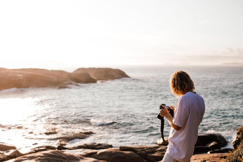 Free A Man Holding a Camera by the Sea  Stock Photo