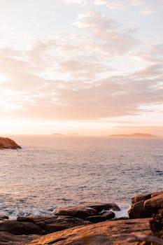 Peaceful sunrise over a rocky seashore with golden light reflecting on the ocean and clouds.