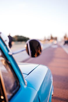 Artistic close-up shot of a vintage blue car's side mirror with a blurred road background.