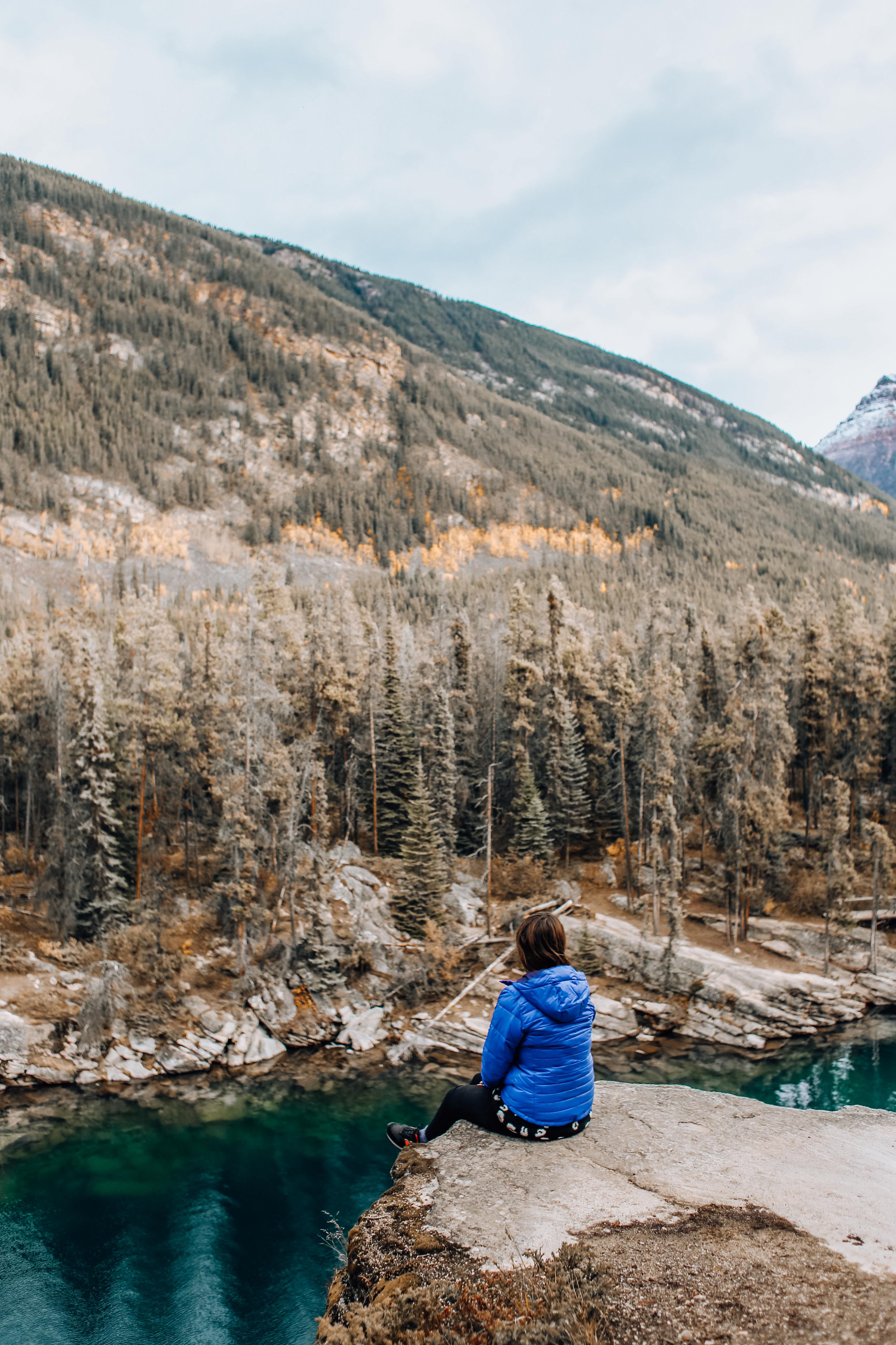 Person in Blue Jacket Sitting on Rock Cliff · Free Stock Photo