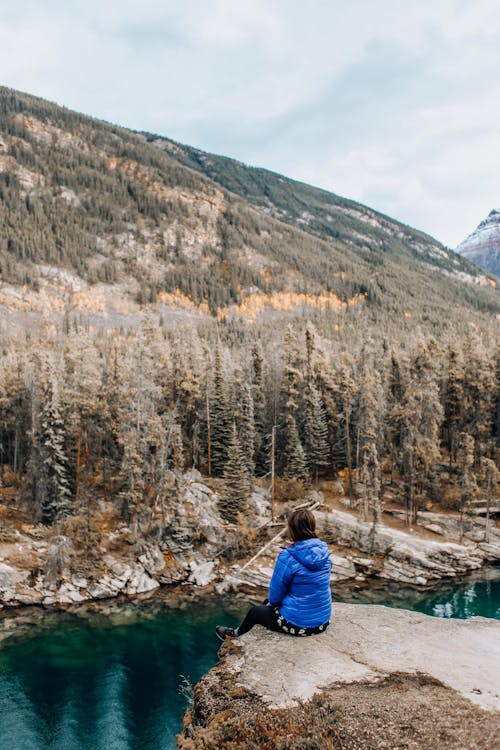 Person in Blue Jacket Sitting on Rock Cliff 