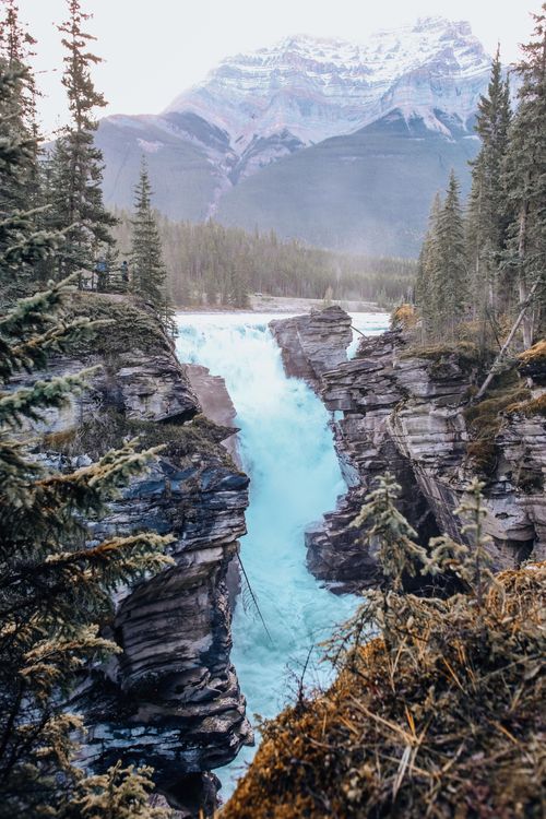 Free Stunning aerial view of a cascading waterfall in a mountain landscape surrounded by lush forest. Stock Photo