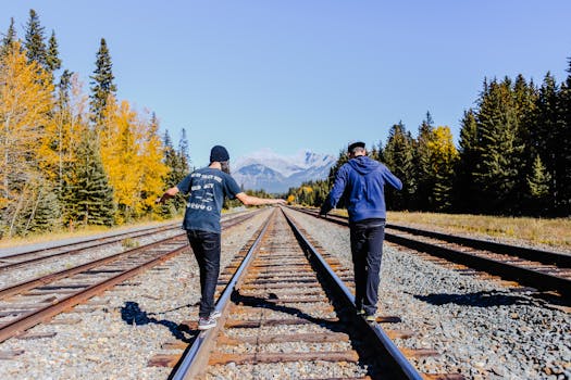 Two friends balancing on railroad tracks surrounded by fall foliage and mountains.