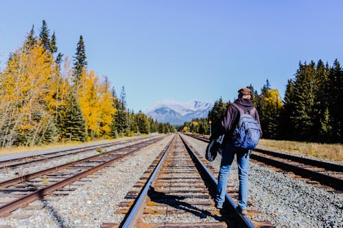 Back View of a Man with Backpack Standing on a Railway