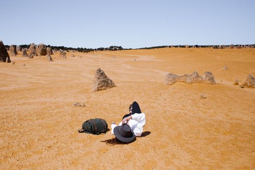 Free A person in a hat relaxes on a sandy desert surrounded by unique rock formations under a clear sky. Stock Photo