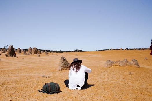 Woman sitting in Australia's Pinnacles Desert under a clear blue sky.