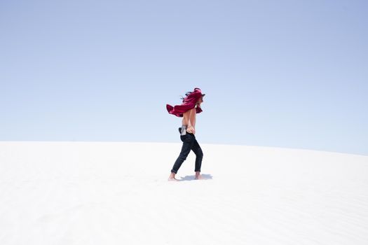 A man walks across bright white desert dunes under a clear summer sky, showcasing a vast landscape.