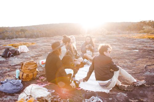 Free A group of friends sitting together outdoors enjoying a sunset picnic on a rocky terrain. Stock Photo