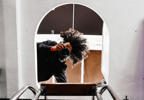 Low angle shot of a photographer holding a camera with curly hair through an arched wall.