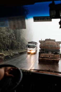 Trucks navigating a foggy mountain road, captured from inside a vehicle, showcasing a misty landscape.