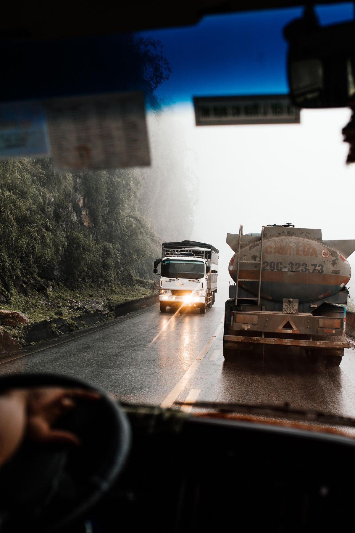 Lorry driving through heavy rain on a Southeast Asian hill road — rain and road grit that wear down lorry sticker surfaces