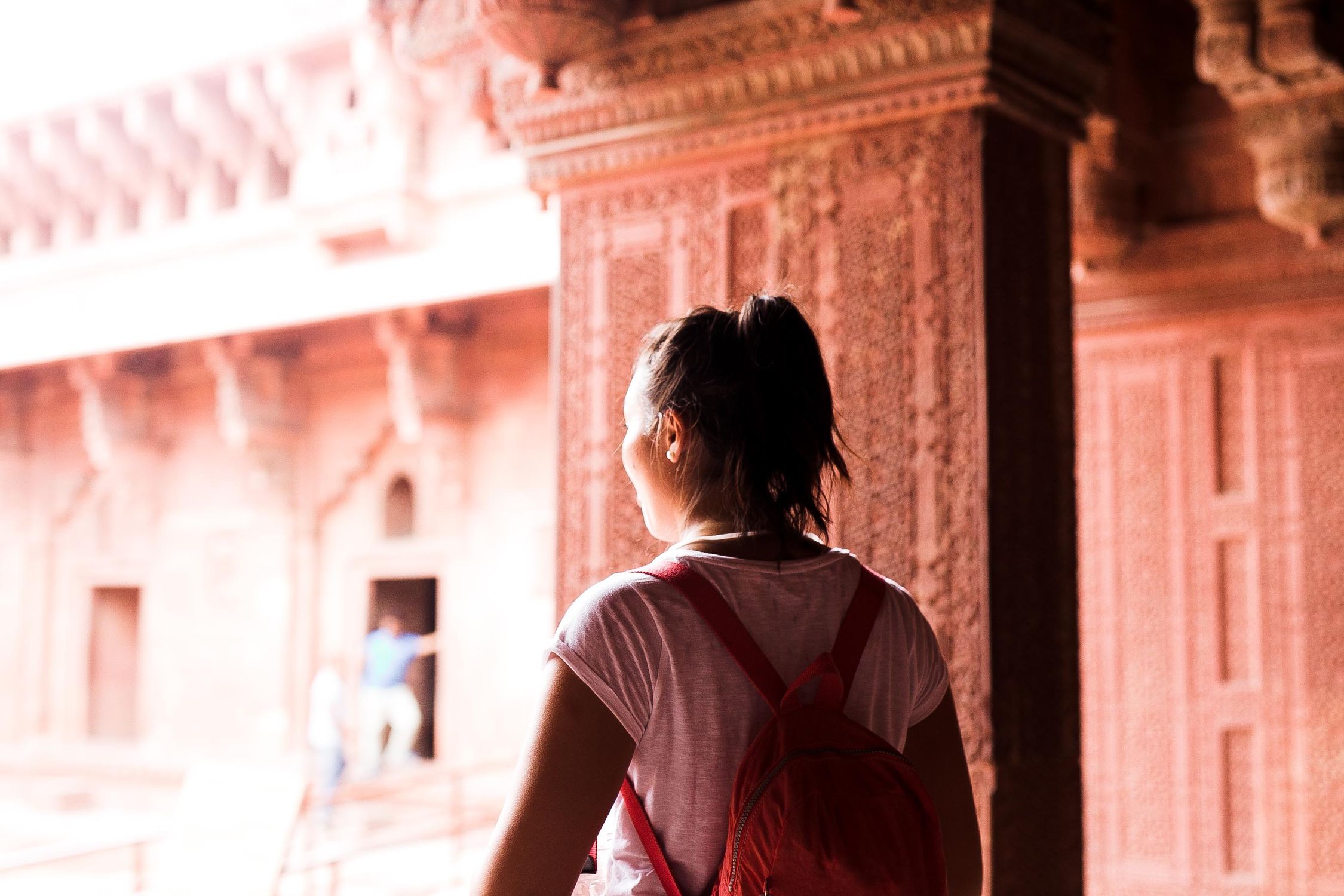 Young female traveler with backpack exploring a historic site. Back view.