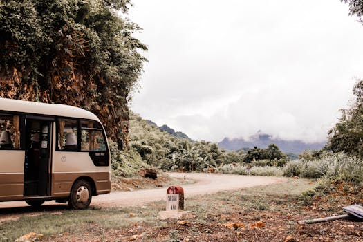 Shuttle bus on a winding road with mountainous backdrop and lush greenery.