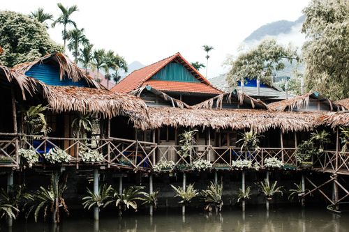 Free Picturesque stilt houses with thatched roofs over water, surrounded by lush greenery. Stock Photo