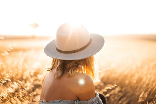 Free A Woman Wearing a Hat Sitting on the Grassland During Sunrise Stock Photo