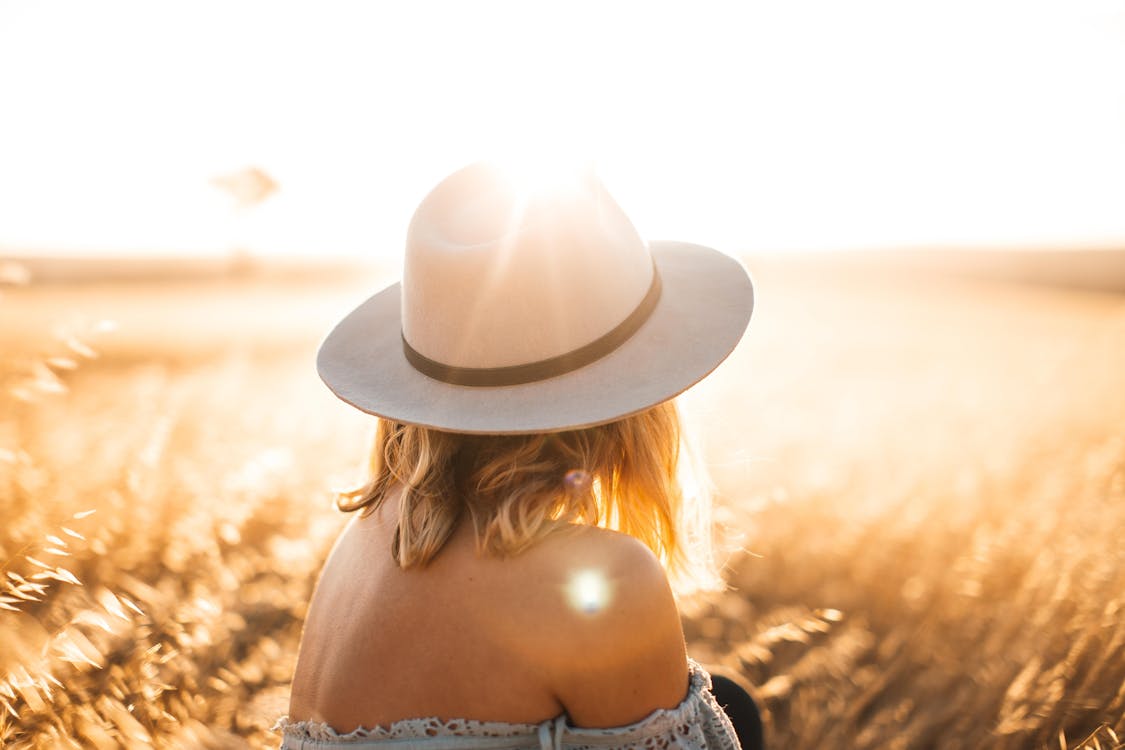 A Woman Wearing a Hat Sitting on the Grassland During Sunrise