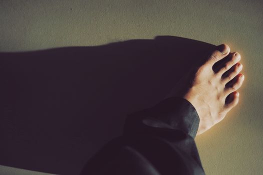 A close-up photo capturing a bare foot casting a dramatic shadow on the ground.