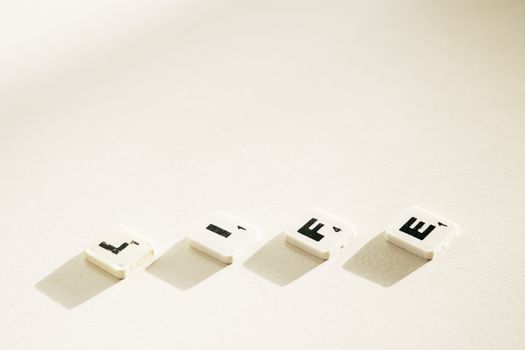Close-up of Scrabble tiles spelling 'Life' with dramatic shadows on a light background.