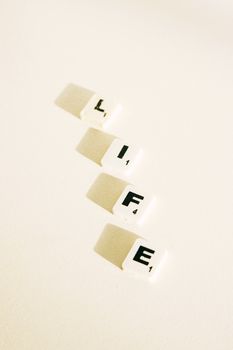 Vertical shot of Scrabble tiles forming the word 'Life' on a white background with shadows.