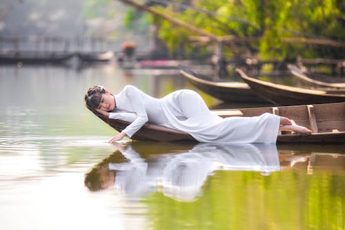 Woman in White Dress Lying on Brown Wooden Boat on River