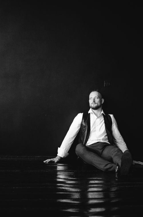 Free Black and white portrait of a man sitting thoughtfully on the floor against a dark background. Stock Photo