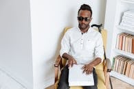 Man in White Dress Shirt Wearing Black Sunglasses Sitting on Brown Wooden Armchair