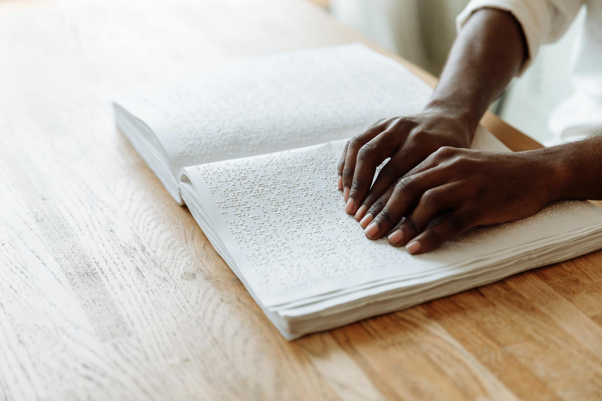 Hands exploring a Braille book on a wooden table, emphasizing accessible learning.