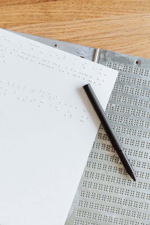 Free A vertical shot of Braille paper and a pen on a wooden table, highlighting tactile writing. Stock Photo