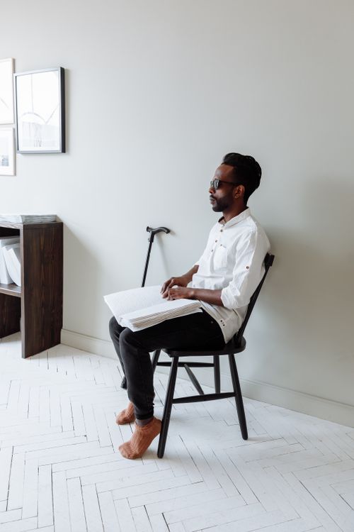 Free A man with a cane reads braille while sitting barefoot indoors. Stock Photo