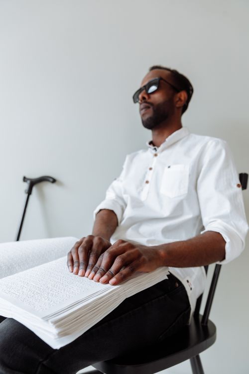 Free African American man in sunglasses reading Braille with focus on tactile engagement. Stock Photo