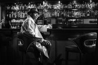 Monochrome Photo of Man Sitting in Front of  Bar Counter
