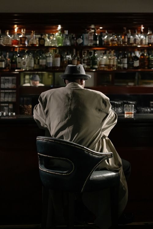 Free Back view of a person in a trench coat sitting at a bar, adding a mysterious allure. Stock Photo