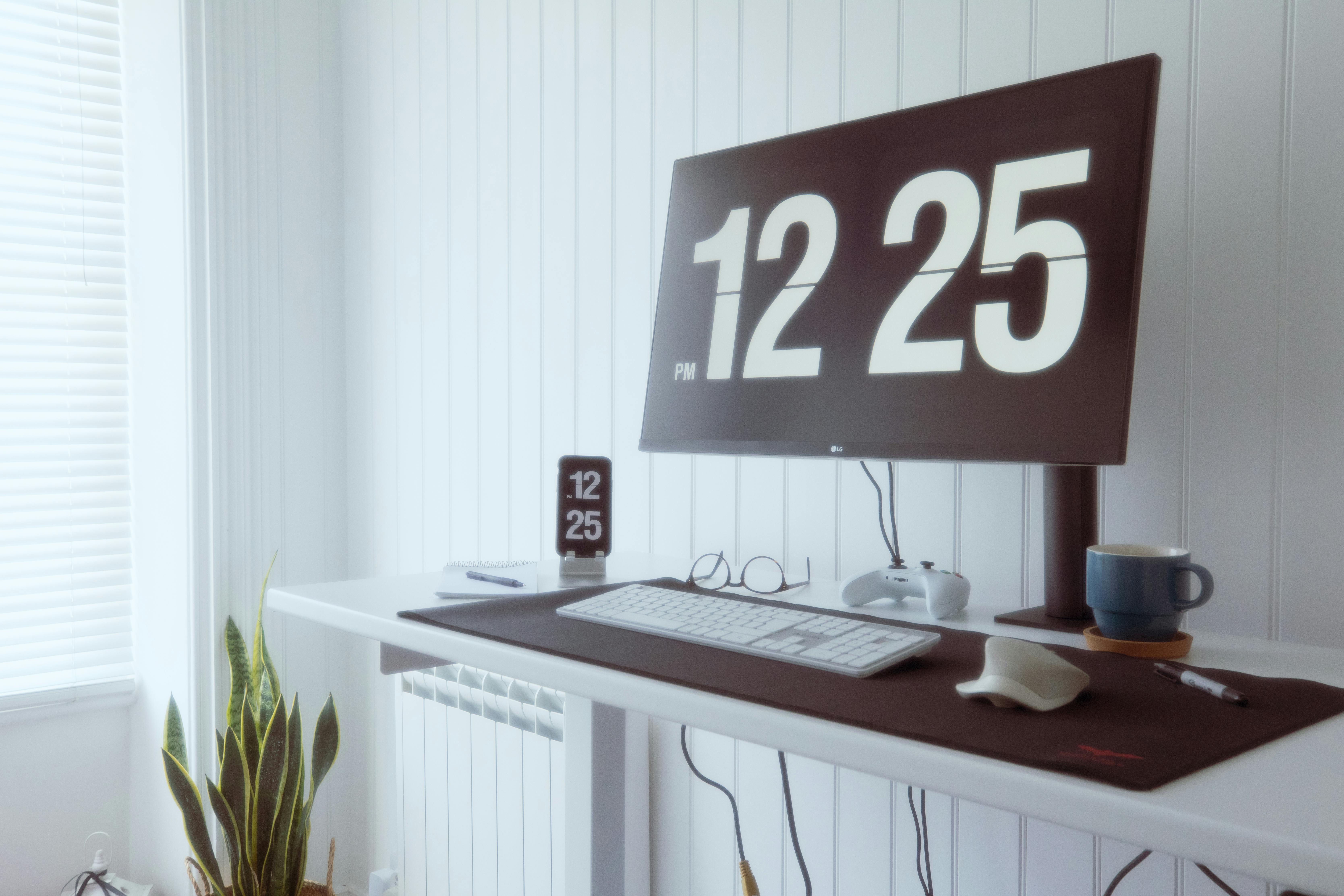 A stylish home office desk setup with a large digital clock display, keyboard, and plant decor.